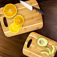 The 2-Piece Striped Bamboo Cutting Board Set by Totally Bamboo showcases the elegance of kitchen accessories with vibrant oranges and ripe avocados on a wooden surface. Crafted from eco-friendly Moso bamboo, these cutting boards add a natural touch of beauty to any culinary space.