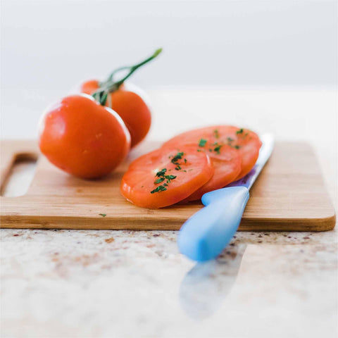 On a sleek marble countertop, the 2-Piece Bamboo Cutting Board Set by Totally Bamboo holds whole vine tomatoes and herb-sprinkled slices. A knife with a blue handle rests nearby, highlighting this kitchen's knife-friendly setup.