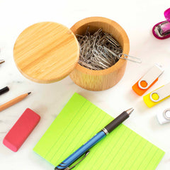 A Totally Bamboo Salt Cellar with Swivel Lid, featuring a 6-ounce capacity, is filled with paper clips and sits open on a desk. It is surrounded by office supplies such as a blue pen, green notepad, two USB drives, an eraser, pencil, and pink stapler.