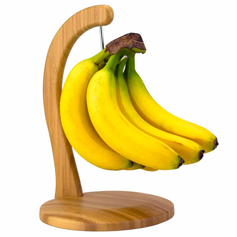 A bunch of yellow bananas hangs gracefully on the Totally Bamboo banana holder, which features a stainless steel hook. The wooden holder showcases a smooth, round base and a curved arm that elegantly highlights the vibrant bananas against a pristine white background.