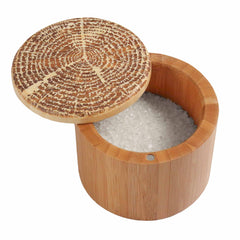 Introducing the Totally Bamboo "Tree of Life" Engraved Salt Cellar, with a 6-ounce capacity. This round wooden salt cellar comes with a magnetic lock lid and is filled with coarse white salt. The partially open lid displays the grains inside and highlights an elegant wood grain pattern, while the container itself showcases a smooth, natural finish.