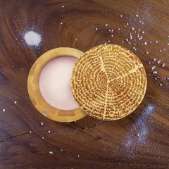 The "Tree of Life" Engraved Salt Cellar by Totally Bamboo, with a 6-oz. capacity, showcases its beautifully crafted decorative lid and reveals the vibrant pink Himalayan salt inside as it sits on a wooden surface sprinkled with additional grains of salt.