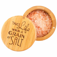 The "Grain of Salt" Engraved Salt Cellar by Totally Bamboo is a round wooden container filled with pink Himalayan salt. It features a swiveling lid, slightly open to reveal the engraved phrase "Take life with a grain of salt," and includes a discreet magnetic lock to ensure secure closure.