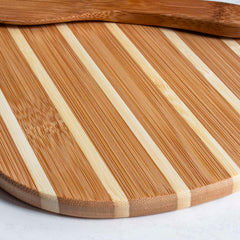 The Pineapple Serving Board with Spreader Knife Gift Set by Totally Bamboo features a round wooden design with alternating light and dark stripes, adding a tropical flair to the white surface. Resting on top is a wooden spatula along with the included bamboo spreader knife, perfect for elevating your island-inspired culinary presentation.