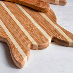 A Sea Turtle Serving Board with a spreader knife from the Totally Bamboo gift set, featuring alternating light and dark stripes, is placed on a light surface. A matching wooden spatula rests gracefully on top.