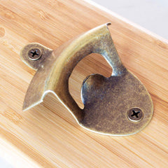 The Totally Bamboo Wall-Mounted Bottle Opener with Magnetic Cap Catcher boasts a vintage brass design and attaches to a wooden surface using two screws. Its distinct curved shape allows for easy opening of bottles, while the magnetic cap catcher ensures your space remains tidy and stylish.