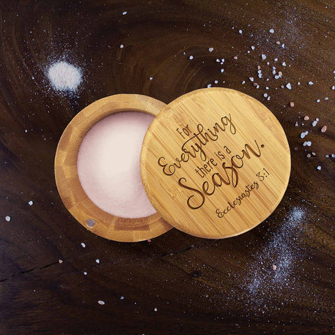 The Totally Bamboo "For Everything a Season" Engraved Salt Cellar, 6-Oz., features a lid with an Ecclesiastes 3:1 quote, making it both elegant and functional. Complete with pink salt inside and scattered granules on a dark surface, this charming wooden container truly stands out.