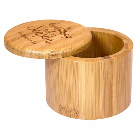 The "For Everything a Season" Engraved Salt Cellar by Totally Bamboo is a round, wooden container with a slightly ajar removable lid. Crafted from bamboo, it features a natural texture and color, with the lid engraved in a decorative font.