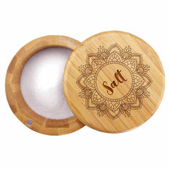 A circular "Mandala Salt" Engraved Salt Cellar by Totally Bamboo, crafted from wood, displays its intricate lid with a mandala pattern and the word "Salt" at the center. Partially open, it reveals white salt inside and features a discreet magnetic lock for secure closure.