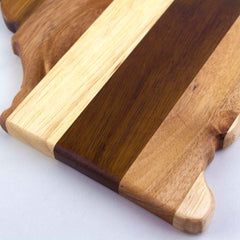 A close-up of the Rock & Branch® Shiplap Series California Cutting Board by Totally Bamboo showcases its craftsmanship with alternating stripes of light and dark wood. The cutting board's irregular, elegantly shaped edge embodies the charm associated with Rock & Branch Shiplap, making it an ideal choice for those who value functional elegance against a white background.