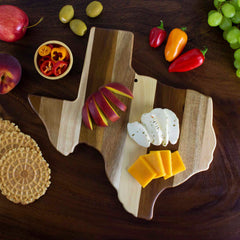 A Rock & Branch® Shiplap Series Texas Cutting Board from Totally Bamboo features an arrangement of assorted cheeses, apple slices, and colorful peppers. The vibrant display is completed with fruits, waffle-like crackers, and grapes on the rich wooden backdrop.