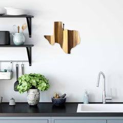 A modern kitchen boasts a sleek countertop and sink, complete with a potted plant and shelves filled with kitchenware. The Texas-shaped Rock & Branch® Shiplap Series Cutting Board by Totally Bamboo highlights the wood plank colors against the white wall.