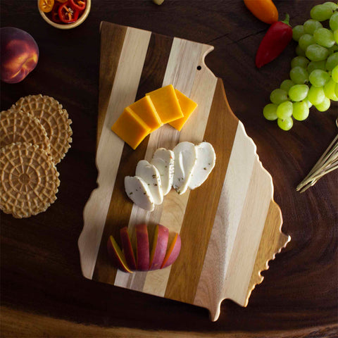 The Rock & Branch® Shiplap Series Georgia Cutting Board by Totally Bamboo, designed to resemble the state of Georgia, beautifully displays sliced cheeses and apple slices. It's artfully accompanied by waffles, grapes, and peppers on a dark surface—ideal for gifting or enhancing your wall art collection.