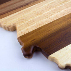 A close-up of the Rock & Branch® Shiplap Series Montana Cutting Board by Totally Bamboo reveals its elegant blend of alternating light and dark wood stripes. With its unique, decorative edge set against a light gray background, this piece exudes the charm and artistic appeal akin to wall art while serving as a practical kitchen tool.