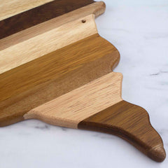 A close-up of the Rock & Branch® Shiplap Series Minnesota Cutting Board by Totally Bamboo showcases its alternating dark and light stripes, set against a white marble surface. Part of the Shiplap Series, this wooden cutting board features a decorative, irregular edge that evokes an artisanal wood plank design.