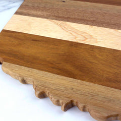 This is an up-close view of the Rock & Branch® Shiplap Series Oklahoma Cutting Board from Totally Bamboo, which highlights a stunning array of wooden strips, each with unique shades and grains. The board features a scalloped edge at the bottom and is gracefully positioned on a white surface.