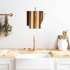 A modern kitchen features a wooden countertop and sink. The copper faucet and handles complement the white cabinetry. Above the sink, the Rock & Branch® Shiplap Series Arkansas Cutting Board by Totally Bamboo, with its wood plank colors, doubles as wall art while a bunch of herbs dangles nearby.