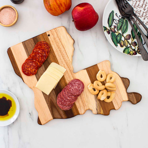 The Rock & Branch® Shiplap Series Louisiana Cutting Board by Totally Bamboo showcases a delightful spread of sliced meats, cheese, and bagels. Nearby, an apple complements plates adorned with salt and olive patterns, complete with ready forks—all set against an elegant Rock & Branch marble background.