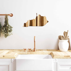 A modern kitchen features a wooden counter and white sink, above which is mounted the Rock & Branch® Shiplap Series Kentucky Cutting Board by Totally Bamboo as a decorative wall art piece. The copper faucet and handles enhance the decor, complemented by a few herbs hanging nearby.