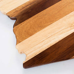 A close-up of the Rock & Branch® Shiplap Series Arizona Cutting Board by Totally Bamboo showcases its alternating light and dark striped pattern. The edge features a rugged design reminiscent of a mountain landscape, all set against a plain white background.