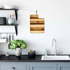 A modern kitchen features a black countertop, light blue cabinets, and a white sink, highlighted by the Shiplap Series backsplash. The Rock & Branch® Shiplap Series Utah Cutting Board by Totally Bamboo hangs on the wall, while shelves display a plant, bowls, and toaster. A potted plant rests on the counter near the sink.