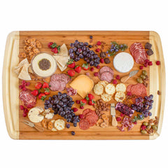 An exquisite 800SI XL Cutting Board & Noodle Board by Totally Bamboo, measuring 36" x 24", showcases an elegant assortment of cheeses, cured meats, crackers, and fruits like grapes and strawberries. Nuts, olives, and a small bowl of dip are expertly arranged for a sophisticated presentation.