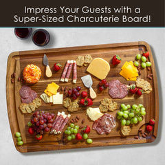 A super-sized charcuterie board, artfully arranged on the Rock & Branch® 600SI Cutting Board & Noodle Board by Totally Bamboo, features an impressive selection of assorted cheeses, meats, fresh grapes, strawberries, and nuts. Two small knives complete the experience alongside nearby glasses of red wine. The text reads, "Impress Your Guests with a Super-Sized Charcuterie Board!