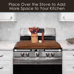 In a kitchen setting, the Rock & Branch® 600SI Cutting Board & Noodle Board by Totally Bamboo is prominently displayed on the stove, accompanied by a utensil holder and a pepper mill. The image underlines that this extra-large board measures 30 inches wide, with text above indicating it provides valuable additional space to your kitchen.