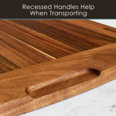 A close-up of the Rock & Branch® 600SI Cutting Board & Noodle Board by Totally Bamboo, featuring recessed handles on a marble surface. The top text reads: "Recessed Handles Help When Transporting." This extra-large 30" x 20" board showcases a smooth finish that accentuates its natural wood grain patterns.