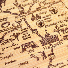 Introducing the Slice of Life Alabama Cutting Board by Totally Bamboo, a detailed hand-drawn map showcasing Alabama's cities, highways, and landmarks. This 11" x 8-3/4" board features illustrations of Birmingham and Montgomery, along with charming depictions of a cow, trees, and roads—highlighted with names such as Tuscaloosa and Talladega National Forest—all intricately set within an enchanting outline of the state.