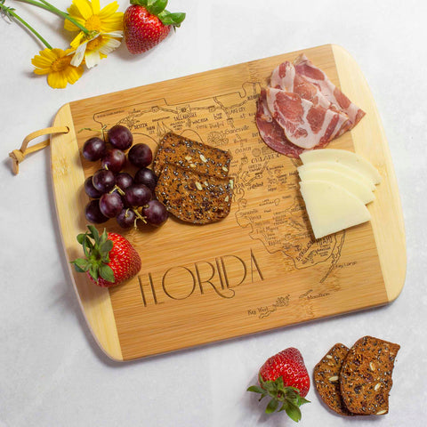 Bamboo cutting board engraved with Florida map and attractions artwork serving charcuterie foods on white textured surface