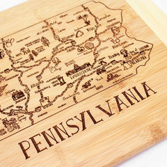 The Totally Bamboo "A Slice of Life Pennsylvania Cutting Board" (11" x 8-3/4") is a bamboo masterpiece that features a detailed laser-engraved map of Pennsylvania. It highlights cities and landmarks, with the word "PENNSYLVANIA" carved prominently underneath—perfect for kitchen decoration or serving charcuterie.