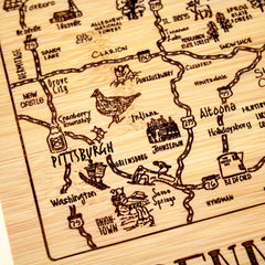 The Totally Bamboo "A Slice of Life Pennsylvania Cutting Board," measuring 11" x 8-3/4", showcases intricately laser-engraved art on wood, highlighting locations in Pennsylvania such as Pittsburgh, Altoona, and Johnstown. This unique piece also features illustrations of local wildlife, like a turkey, paired with roads and city names.