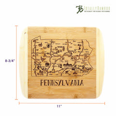 The "A Slice of Life Pennsylvania Cutting Board" by Totally Bamboo is a bamboo cutting board with laser-engraved artwork depicting a map of Pennsylvania, highlighting notable cities and landmarks. Ideal for serving charcuterie, the board measures 11 inches by 8 3/4 inches and features the Totally Bamboo logo in the top right corner.