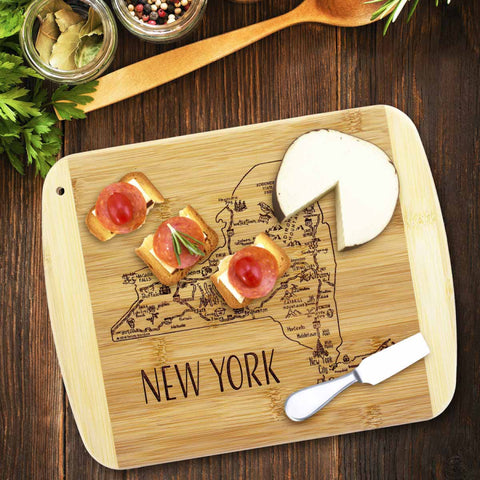 Included in the Totally Bamboo's A Slice of Life Collection, this 11" x 8-3/4" New York cutting board is crafted from bamboo and showcases laser-engraved artwork depicting the state. The design features a round cheese that's been sliced open alongside three small sandwiches garnished with cherry tomatoes and rosemary, complemented by surrounding herbs, spices, and a wooden spoon.