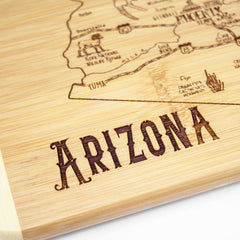 Introducing the "A Slice of Life Arizona Cutting Board" by Totally Bamboo, featuring an intricate engraving of Arizona's outline with cities like Phoenix and Yuma. The word "ARIZONA" is prominently etched at the bottom, making this 11" x 8-3/4" cutting board a perfect state-themed addition to your kitchen.