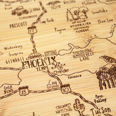 The "A Slice of Life Arizona Cutting Board" by Totally Bamboo, measuring 11" x 8-3/4", serves as both a state-themed cutting board and a decorative wooden map carving. It features prominent locations such as Phoenix at the center, with Scottsdale and Tempe nearby. The design also includes highways and natural landmarks like Theodore Roosevelt Lake, enhancing the charm of this bamboo charcuterie board.