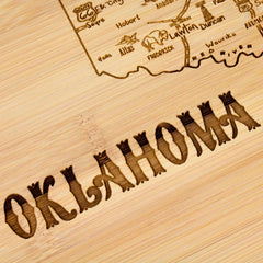 The "A Slice of Life Oklahoma Cutting Board" by Totally Bamboo, measuring 11" x 8-3/4", serves as a charming charcuterie board, featuring intricately engraved cities and landmarks. The word "OKLAHOMA" stands out boldly, blending functionality with state outline artwork to create a distinct design.