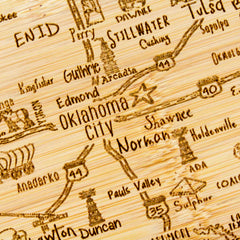 A detailed view of the A Slice of Life Oklahoma Cutting Board by Totally Bamboo, measuring 11" x 8-3/4", highlights part of Oklahoma with cities such as Oklahoma City, Norman, Stillwater, and Tulsa finely engraved onto its surface. The intricate state outline is further enhanced with highway numbers and small decorative icons.