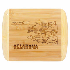 The "A Slice of Life Oklahoma Cutting Board" by Totally Bamboo features a detailed engraving of a map highlighting cities and landmarks across Oklahoma. The design is enhanced with the word "OKLAHOMA" carved beneath the state outline. The board measures 11" x 8-3/4".