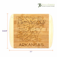 The "A Slice of Life Arkansas Cutting Board" by Totally Bamboo serves as both a bamboo cutting board and a charcuterie serving piece, featuring an engraved map of Arkansas that highlights cities and landmarks such as Little Rock and the Arkansas River. Measuring 11 inches by 8-3/4 inches, it elegantly displays the Totally Bamboo brand at the top right corner.