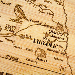 This beautifully crafted laser-etched wooden map, part of Totally Bamboo's A Slice of Life Collection, showcases cities in Nebraska—such as Lincoln, Omaha, and Fremont—on an 11" x 8-3/4" bamboo cutting board. Adorned with a bird illustration near Grand Island and featuring small towns and highway markers, it's perfect for serving charcuterie with a unique touch.