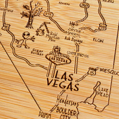 The A Slice of Life Nevada Cutting Board by Totally Bamboo is a one-of-a-kind kitchen accessory, featuring an intricately carved map of Las Vegas with Boulder City and Lake Mead. It's adorned with details like roads, trees, a small alien figure, and a cactus. Both functional and decorative, it's ideal for serving charcuterie at gatherings.