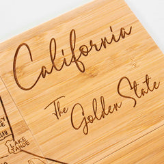 Close-up of a wooden coaster from the Totally Bamboo 4-Piece California Puzzle Coaster Set with Case, showcasing laser-engraved words "California" and "The Golden State" in elegant cursive. A section of a map highlighting "Lake Tahoe" appears on the left, adding a distinctive touch to any puzzle coaster collection.