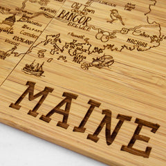 This laser-engraved creation showcases a wooden depiction of Maine, complete with detailed representations of cities and landmarks. Decorative features like a sailing ship add to its appeal, and the word "MAINE" is prominently featured, making it an ideal addition to your 4-Piece Maine Puzzle Coaster Set from Totally Bamboo.