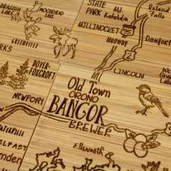 Introducing the Totally Bamboo 4-Piece Maine Puzzle Coaster Set with Case, showcasing a beautifully crafted wooden design of central Maine. It highlights towns such as Bangor, Orono, Lincoln, and Newport. Each coaster is laser-engraved with artistic representations of the local wildlife like moose and birds, as well as routes and symbols reflecting the region's unique charm.