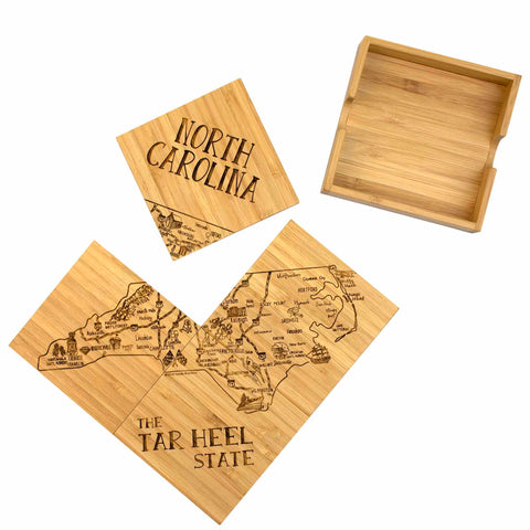 This 4-Piece North Carolina Puzzle Coaster Set with Case, crafted by Totally Bamboo, includes bamboo coasters featuring laser-engraved artwork of a North Carolina map along with the text "The Tar Heel State." One coaster prominently showcases "North Carolina" in a vertical design. The set comes complete with a wooden holder, making it an ideal gift choice.