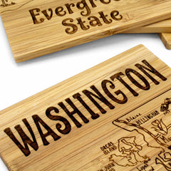 Close-up of the 4-Piece Washington Puzzle Coaster Set with Case by Totally Bamboo, showcasing wooden placards intricately laser-engraved with "Washington" and "Evergreen State." These unique coasters feature artistic designs, including a map, notable landmarks, and the state's outline.