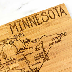 This laser-engraved artwork is a 4-piece Minnesota puzzle coaster set by Totally Bamboo, featuring a wooden design with a detailed map of Minnesota. It showcases key locations such as Duluth, Boundary Waters, and Voyageurs National Park. The illustrations include a wolf and a lighthouse, with "MINNESOTA" etched at the top—an ideal addition for coaster gift enthusiasts.