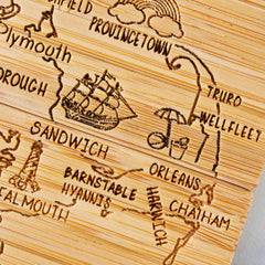 Introducing the 4-Piece Massachusetts Puzzle Coaster Set with Case from Totally Bamboo, a beautifully crafted wooden design featuring intricate laser-engraved artwork of Cape Cod towns such as Sandwich, Barnstable, and Provincetown. Adorned with charming details like a ship, umbrella, and rainbow, this unique piece not only decorates your table but also serves as versatile coasters.